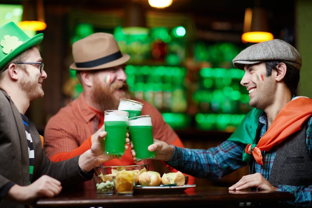 Group of friends enjoying green beer and snacks in a festive pub, celebrating together with smiles and a vibrant atmosphere.
