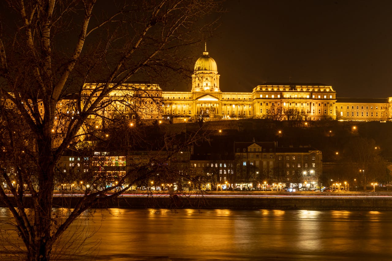 A breathtaking night view of the illuminated Buda Castle in Budapest, with its golden glow reflecting on the Danube River, showcasing the charm of Party Bus Budapest tours.