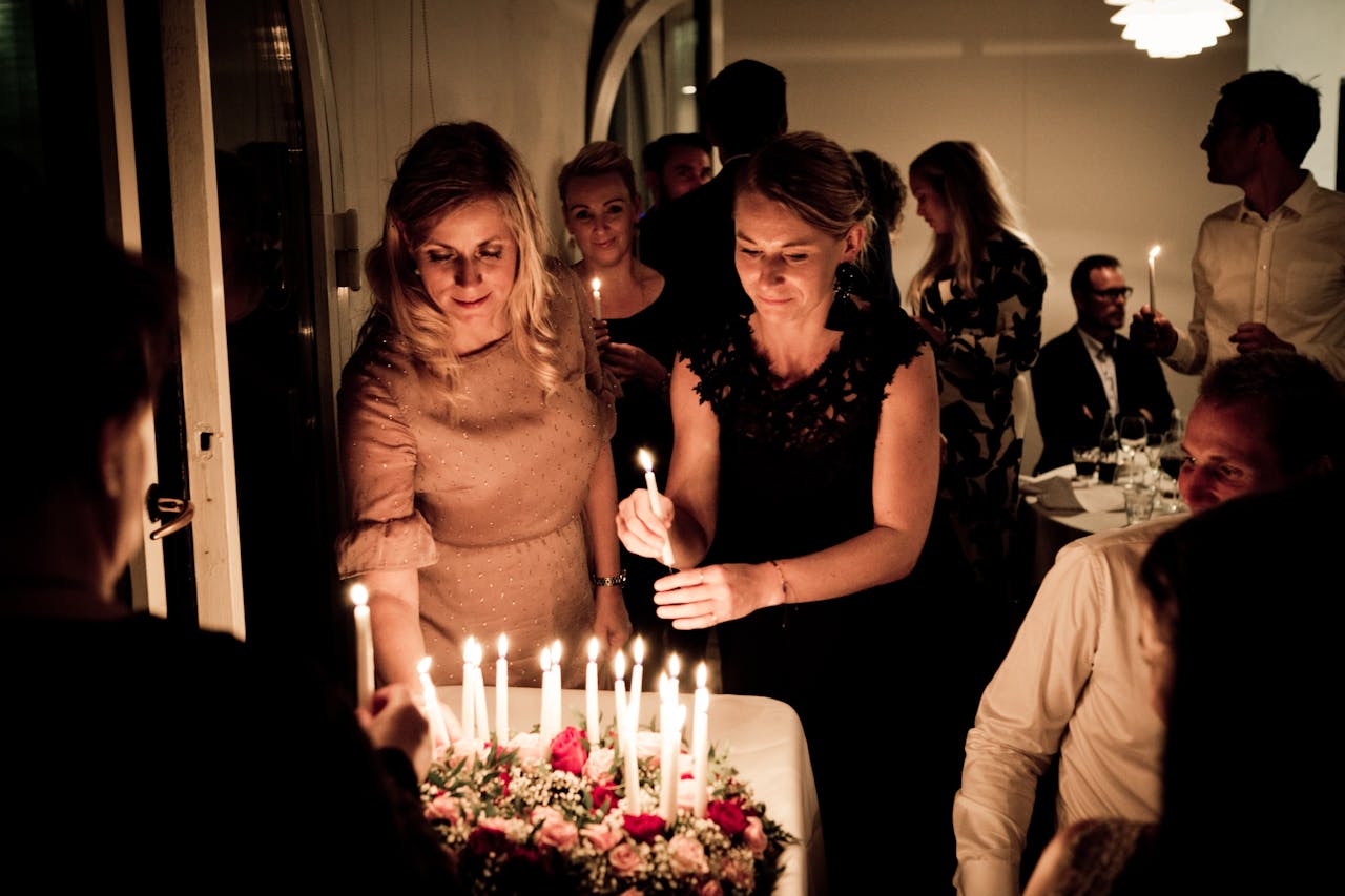 People gathered in an elegant setting, lighting candles on a beautifully decorated table with flowers, creating a warm and festive atmosphere for a special celebration.