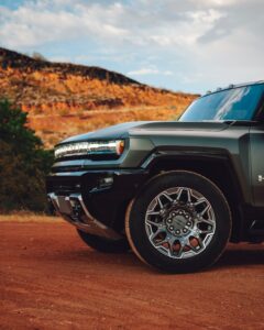 Close-up of a rugged and stylish Green Metal Hummer parked on a red dirt road with scenic autumn hills in the background. Featuring bold design, high-performance wheels, and cutting-edge details, this powerhouse vehicle embodies strength and luxury, making it an ideal choice for a premium limousine experience.