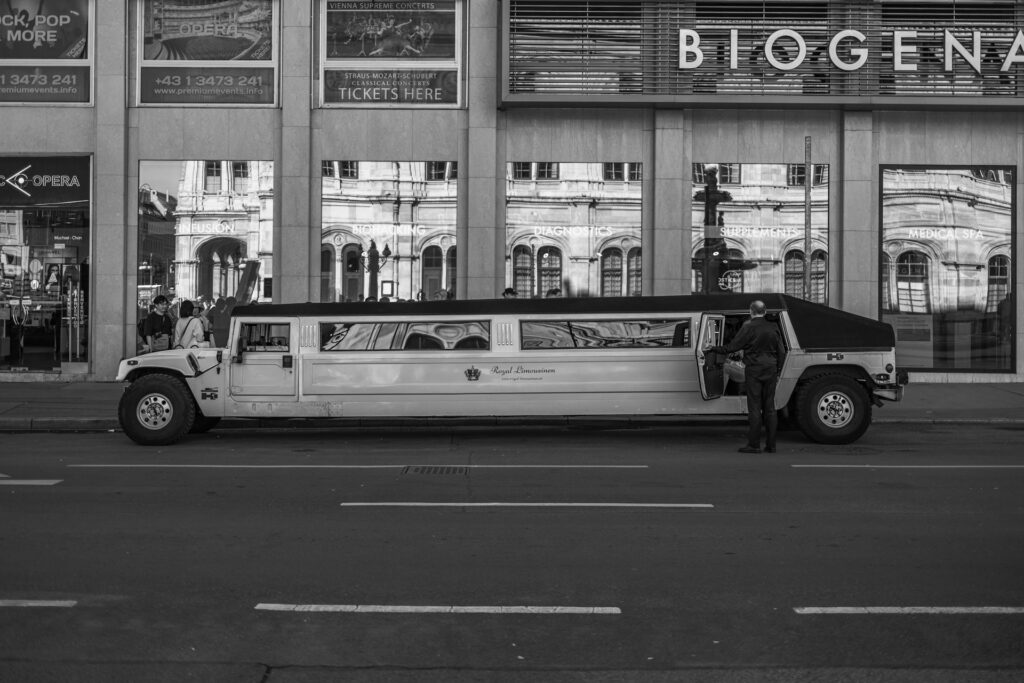 White stretch limousine parked on a city street with driver opening the door for passengers.