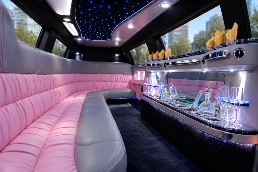 Cadillac limo interior with pink and grey leather seating, a mirrored bar and blue ceiling lights.